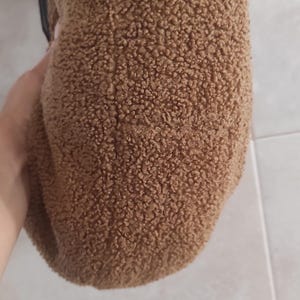 May include: A brown, textured hat with a soft, fuzzy appearance. The hat is a solid color and appears to be made of a plush material. The hat is held by a person.