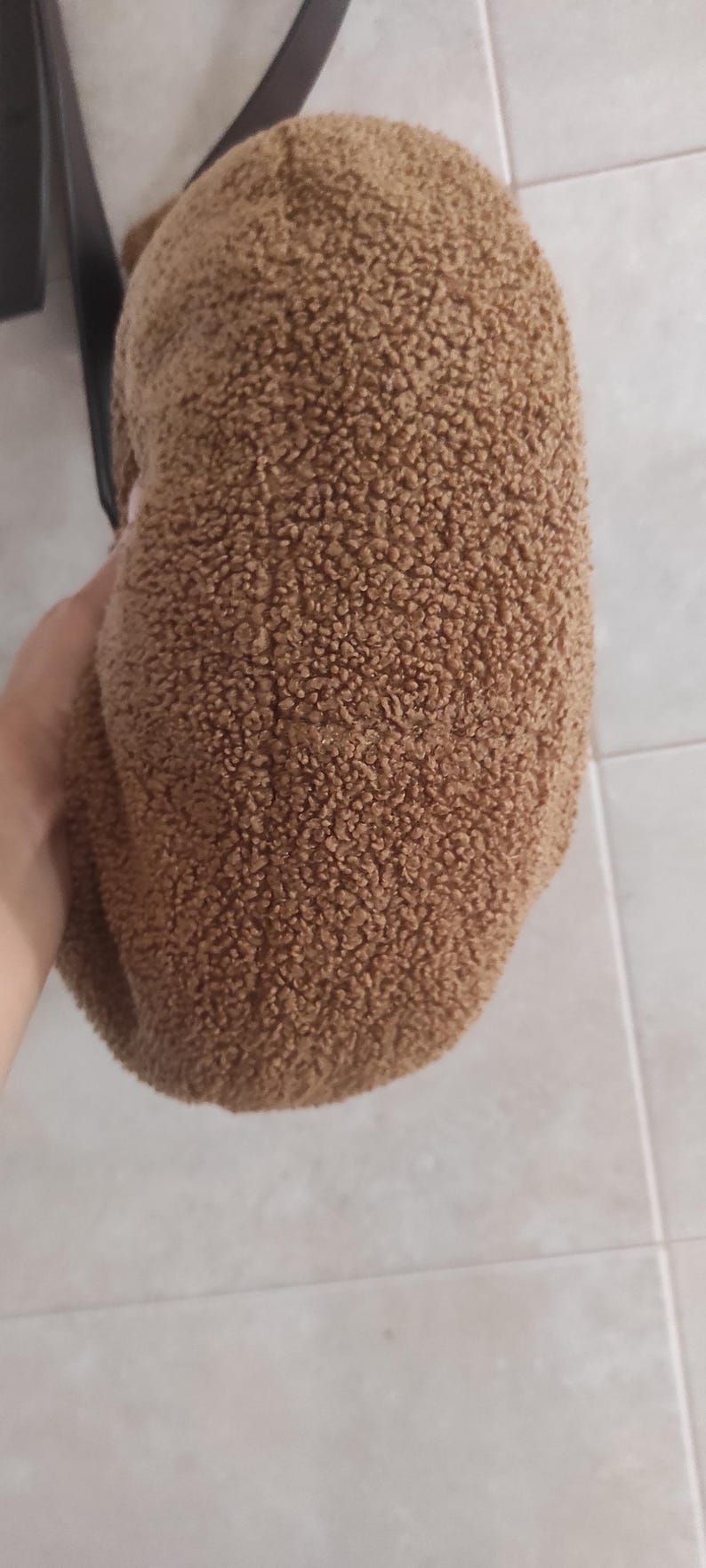 May include: A brown, textured hat with a soft, fuzzy appearance. The hat is a solid color and appears to be made of a plush material. The hat is held by a person.