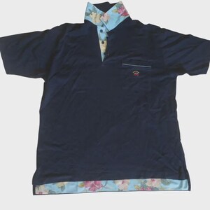 May include: Navy blue polo shirt with a floral patterned collar and hem. The collar and hem feature a light blue background with pink and yellow flowers. A small pocket is on the left chest.