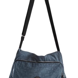 Peut inclure: Un sac à bandoulière en nylon bleu avec une bandoulière réglable noire et un logo circulaire avec le mot "Kipling" dessus.