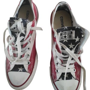 May include: Pair of Converse All Star sneakers. The shoes feature a red, white, and blue color scheme with a star pattern on the tongue and inner lining. White laces and a white rubber toe cap complete the design. The Converse logo is visible.