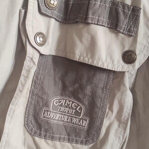 May include: A close-up of a gray and beige jacket with a pocket featuring the text "C.T. Trophy Adventure Wear".