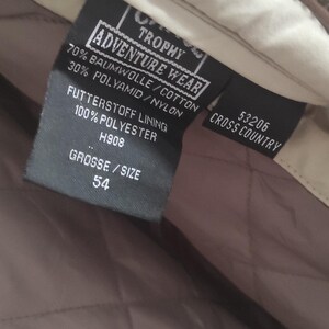 May include: A black label with white text that reads "Adventure Wear Trophy" and "Cross Country 53206". The label also includes details about the fabric composition: 70% cotton, 30% nylon, and a lining made of 100% polyester. The size is indicated as "54".