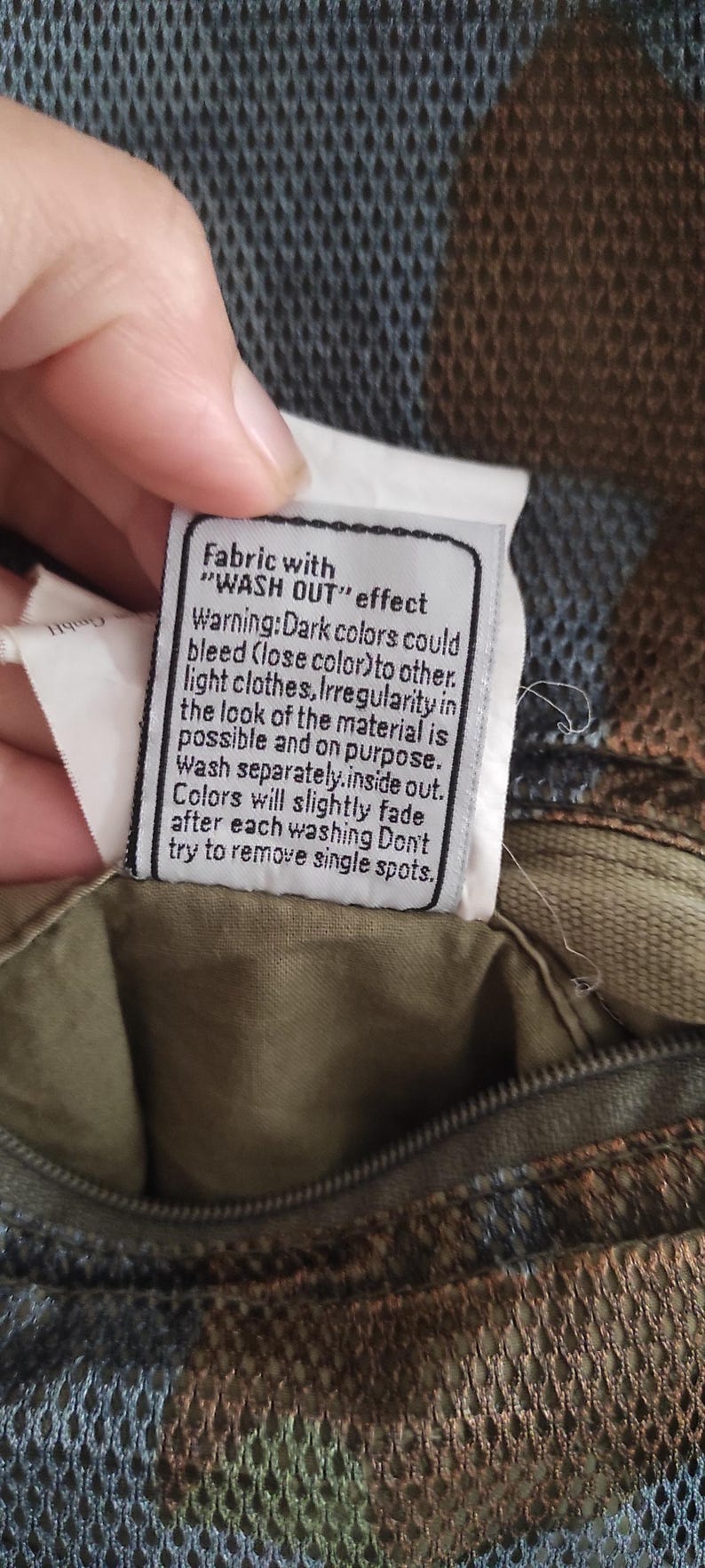 May include: A white fabric care label with black text that reads "Fabric with "WASH OUT" effect. Warning: Dark colors could bleed (lose color) to other light clothes. Irregularity in the look of the material is possible and on purpose. Wash separately. Inside out. Colors will slightly fade after each washing. Don't try to remove single spots."