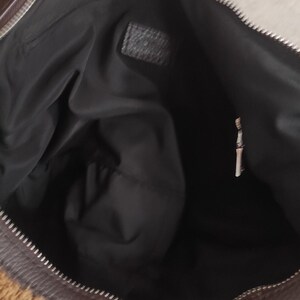 May include: A brown and tan handbag with a zipper closure. The bag has a fuzzy, textured exterior and a black interior. The zipper is silver. The bag is open, revealing the interior.