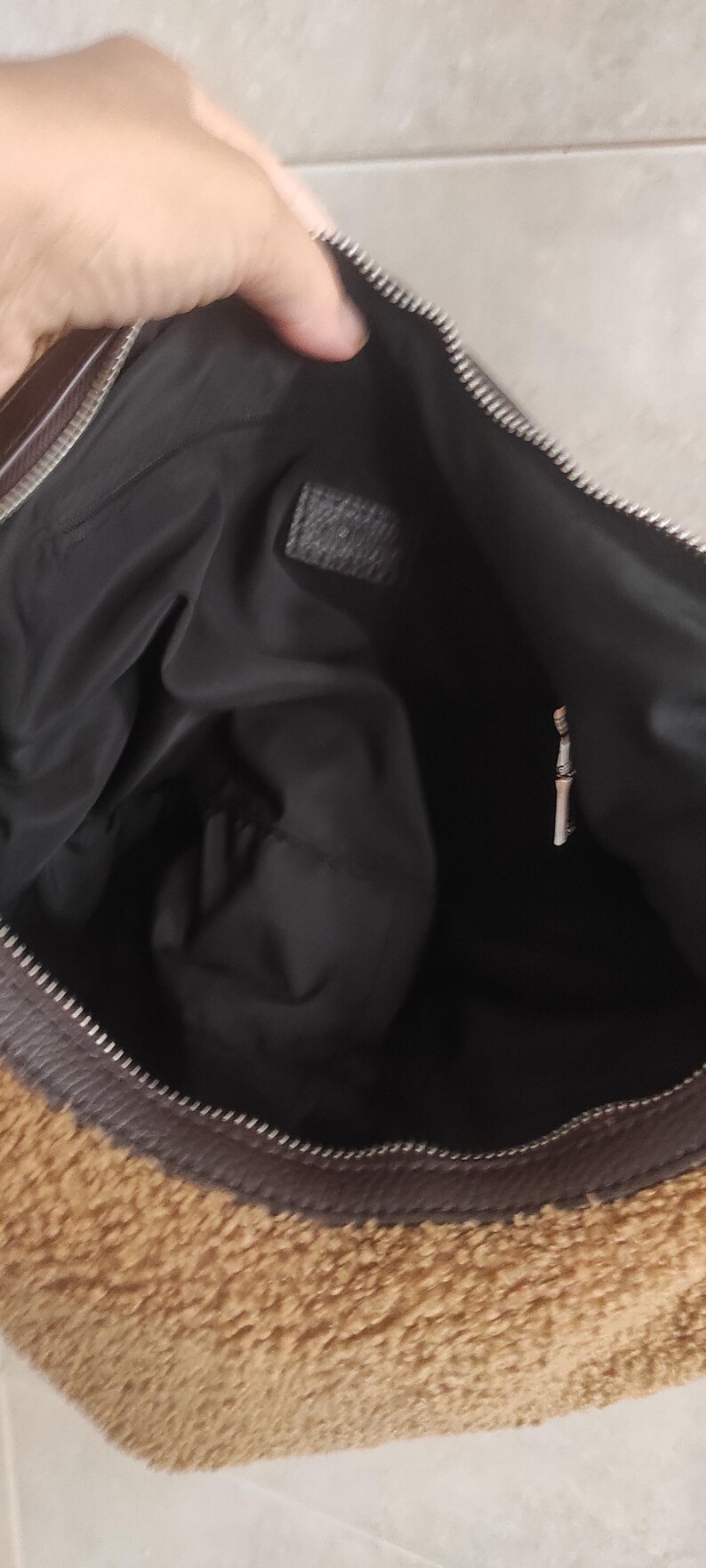 May include: A brown and tan handbag with a zipper closure. The bag has a fuzzy, textured exterior and a black interior. The zipper is silver. The bag is open, revealing the interior.