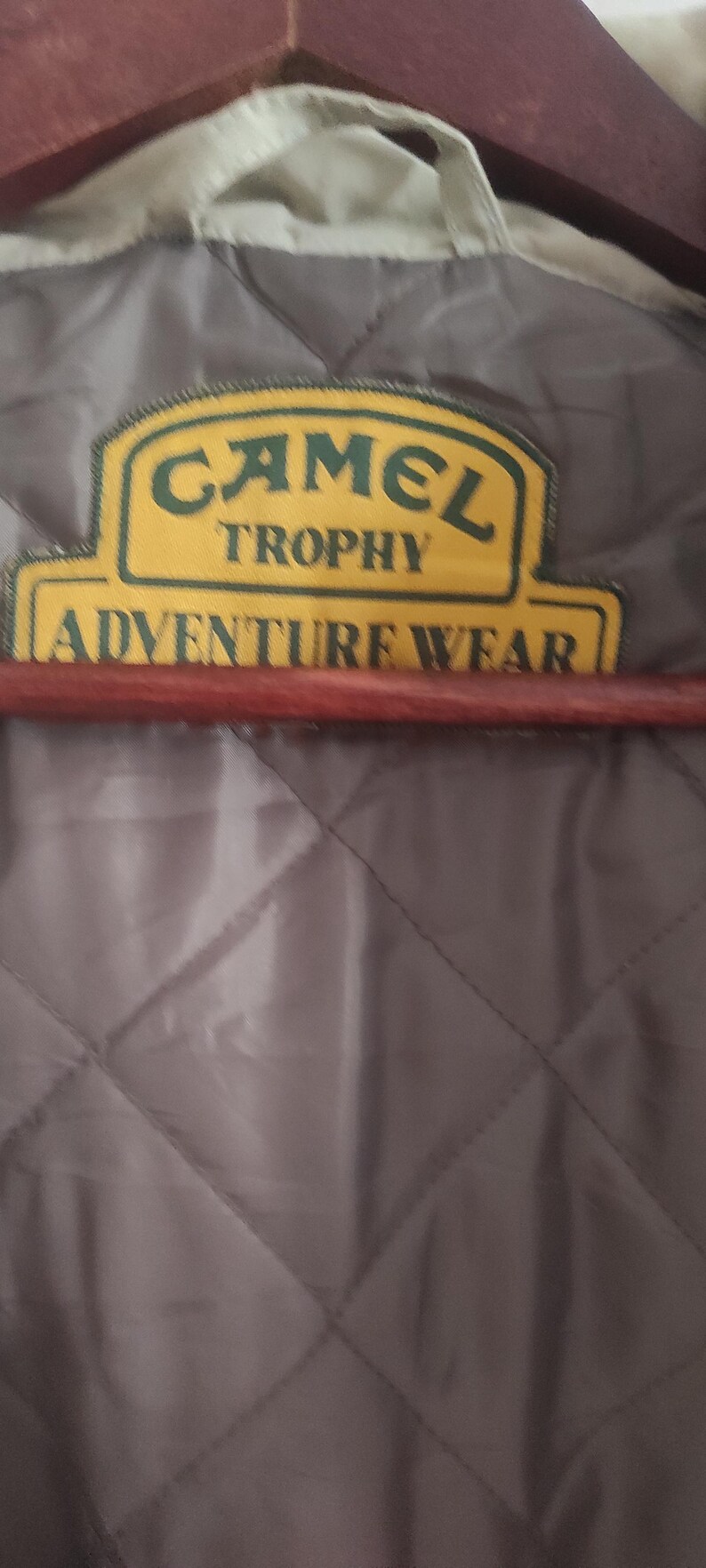 May include: A close-up of a gray quilted jacket with a yellow and green patch that reads "Camel Trophy Adventure Wear".