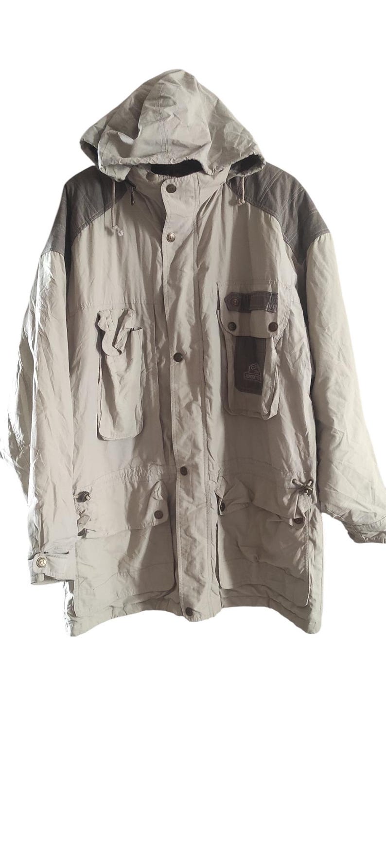 May include: A beige hooded jacket with brown accents and multiple pockets. The jacket has a button closure and a drawstring at the waist.