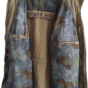 May include: A khaki green vest with a camouflage lining. The vest has a zipper closure and two pockets. The lining has the text "Authentic Heritage" printed on it.