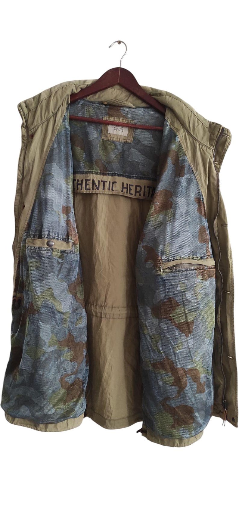 May include: A khaki green vest with a camouflage lining. The vest has a zipper closure and two pockets. The lining has the text "Authentic Heritage" printed on it.