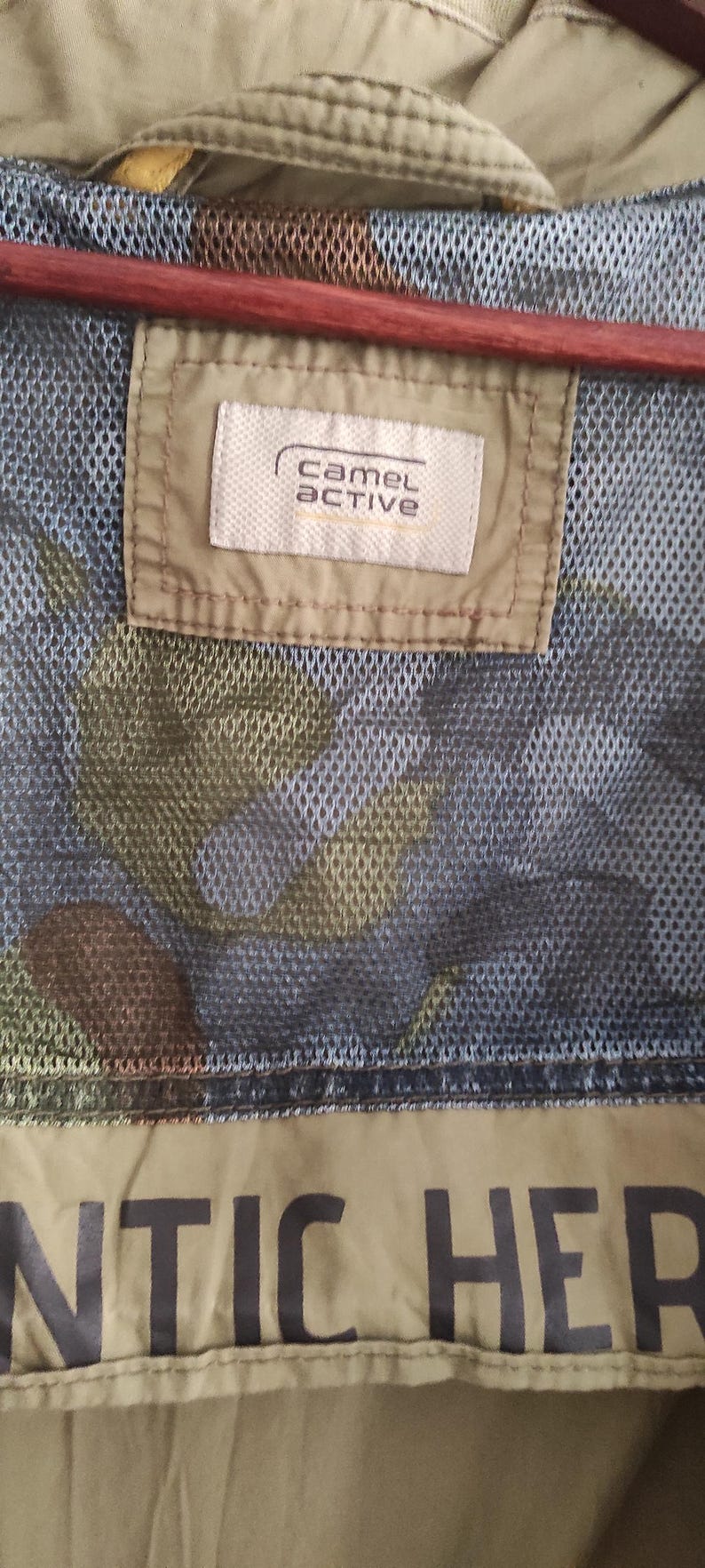 May include: A green camouflage jacket with a brown mesh lining and a white label that says "camel active". The jacket has a black "ANTIC HER" text on the bottom.