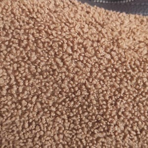 May include: Close-up of a brown, textured handbag. The bag has a soft, fuzzy exterior and a dark brown strap. The bag's material has a plush, teddy bear-like appearance.