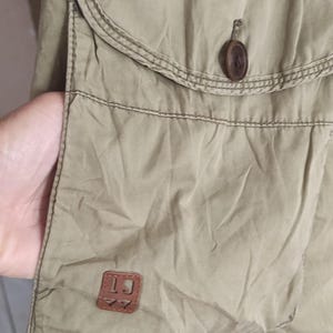 May include: A khaki cargo skirt with a large pocket on the front. The pocket has a brown leather patch with the letters "LJ" on it. There is a button on the pocket flap.