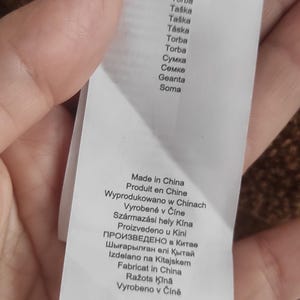 May include: A white product tag with text in multiple languages, including English, French, and German. The tag lists the product's origin as Made in China and includes the brand name s.Oliver. The tag also has a product code and other details.
