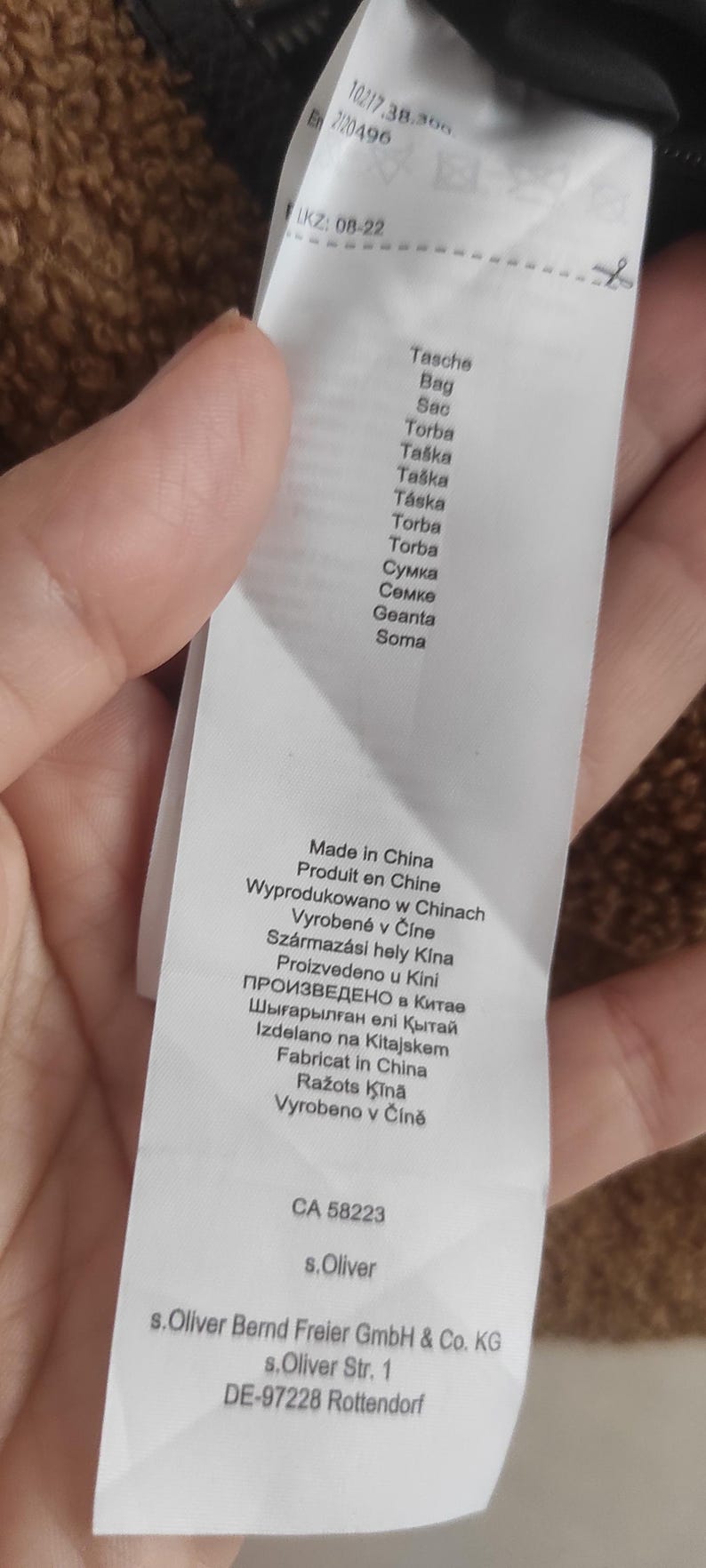 May include: A white product tag with text in multiple languages, including English, French, and German. The tag lists the product's origin as Made in China and includes the brand name s.Oliver. The tag also has a product code and other details.