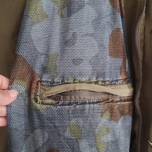 May include: A brown and green camouflage jacket with a zippered pocket on the sleeve. The pocket has a mesh lining.