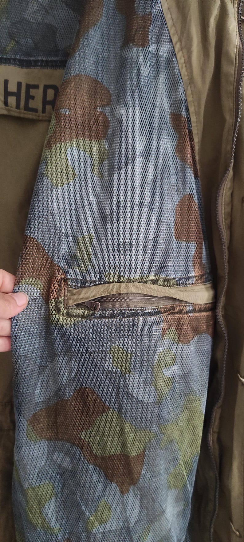 May include: A brown and green camouflage jacket with a zippered pocket on the sleeve. The pocket has a mesh lining.