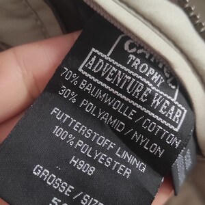 May include: A black label with white text that reads "Adventure Wear Trophy" and "70% Baumwolle/Cotton 30% Polyamid/Nylon" and "Futterstoff Lining 100% Polyester" and "H908" and "Grosse/Size 54".