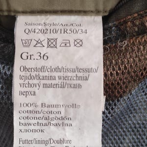 May include: A white clothing label with black text and care instructions. The label says "Saison/Style/Art./Col. Q/420210/1R50/34" and "Gr. 36". The label also includes instructions for washing and ironing the garment.