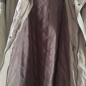 May include: A beige and brown jacket with a quilted lining. The jacket has a zipper closure and a label that reads "Camel Trophy Adventure Wear".