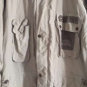 May include: A beige hooded jacket with brown accents and a patch that reads "Cameo Trophy Adventure Wear".