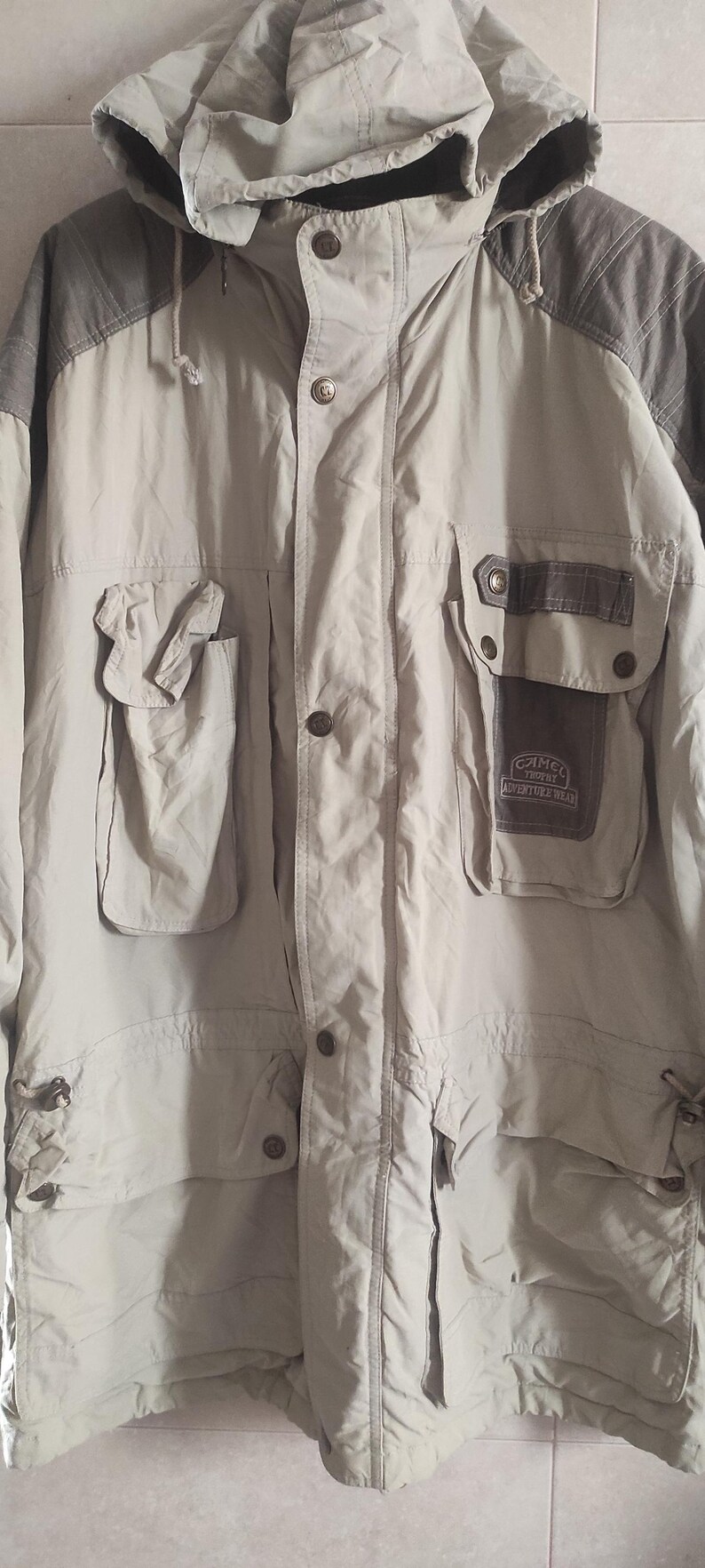 May include: A beige hooded jacket with brown accents and a patch that reads "Cameo Trophy Adventure Wear".