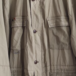 May include: A beige utility jacket with multiple pockets and a button closure. The jacket has a brand label that reads "Camel" on the front.
