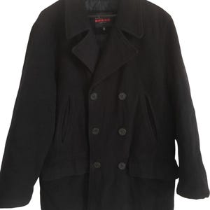 May include: A black double-breasted wool coat with a notched collar and six dark buttons. The coat has two front pockets and a label that reads "SPORT". The coat is hanging on a wooden hanger.
