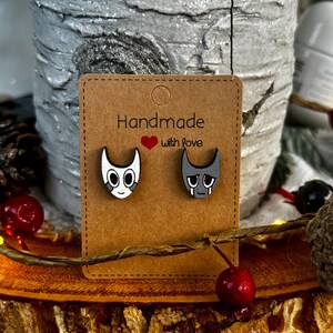 Puede incluir: Pendientes de madera con dos caras de dibujos animados, una feliz y otra triste, presentados en una tarjeta marr&oacute;n. La tarjeta dice "Handmade with love".