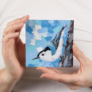 Peut inclure: Peinture à l'huile carrée d'une sittelle torchepot sur une branche d'arbre. L'oiseau a une tête noire et blanche et des ailes bleues. Le fond est un mélange texturé de coups de pinceau bleus et blancs.