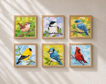 Op de afbeelding: Een set van zes vierkante ingelijste schilderijen met kleurrijke vogels, waaronder een bruine winterkoning, een zwartkopmees, een blauwe vogel, een gele putter, een blauwe gaai en een rode kardinaal, elk zittend op een tak tegen een textuurrijke achtergrond.