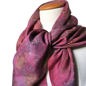 Könnte beinhalten: Ein Seidentuch in Rosa- und Lilatönen mit einem Batik-Muster. Das Tuch ist um den Hals einer weißen Puppe gebunden.