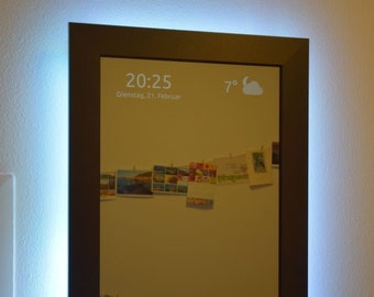 May include: A smart mirror with a black frame and a white LED light around the edge. The mirror displays the time, date, and temperature. It also shows a cloud icon and the text "Too Close For Comfort" by Mel Torme.