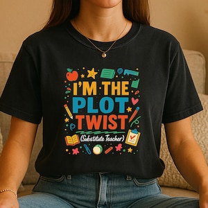May include: Black t-shirt with a colorful graphic that reads "I'M THE PLOT TWIST (Substitute Teacher)". The design includes an apple, stars, pencils, and other school-themed illustrations. The shirt is made of a soft material.