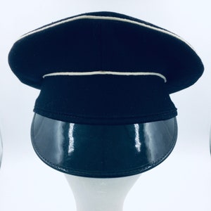 May include: A black peaked cap with a white band around the crown and a black patent leather visor.