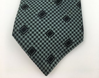 Puede incluir: Una corbata de patrón verde y negro con un diseño geométrico. La corbata tiene una punta puntiaguda y está hecha de un material sedoso.