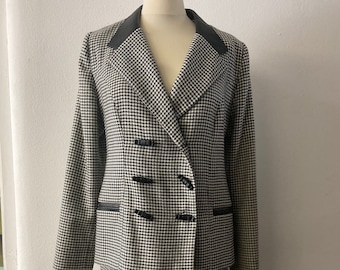 May include: A black and white houndstooth patterned skirt suit with a double-breasted jacket and a black collar.