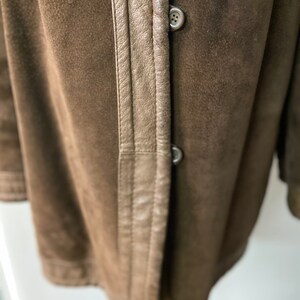 May include: Close-up of a brown suede jacket with a brown leather trim and two buttons. The jacket has a classic design and a soft, luxurious feel.