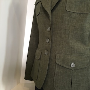 Op de afbeelding: Een groene blazer met knoopsluiting en meerdere zakken. De blazer heeft een textuur in de stof en een klassieke stijl.