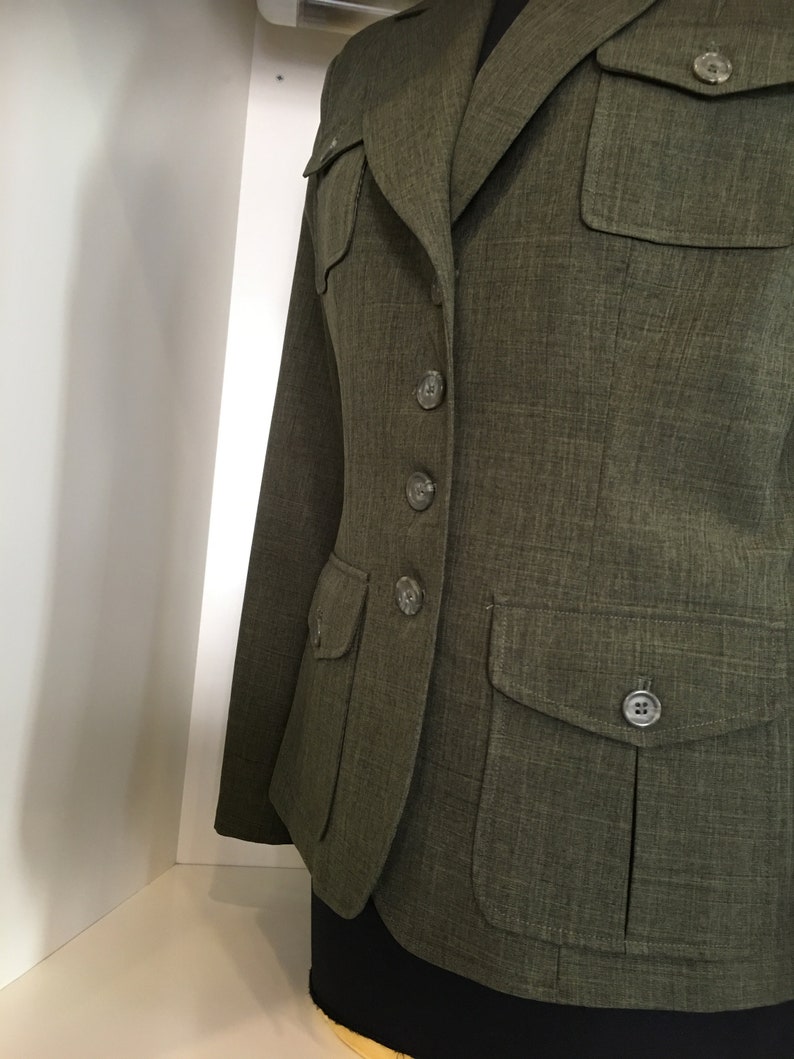 Op de afbeelding: Een groene blazer met knoopsluiting en meerdere zakken. De blazer heeft een textuur in de stof en een klassieke stijl.