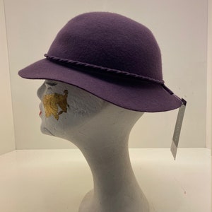 May include: A purple felt hat with a braided trim. The hat is on a white mannequin head.
