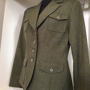 Op de afbeelding: Een groene blazer met knoopsluiting en twee grote zakken aan de voorkant. De blazer heeft een textuur in de stof en een aansluitende pasvorm.