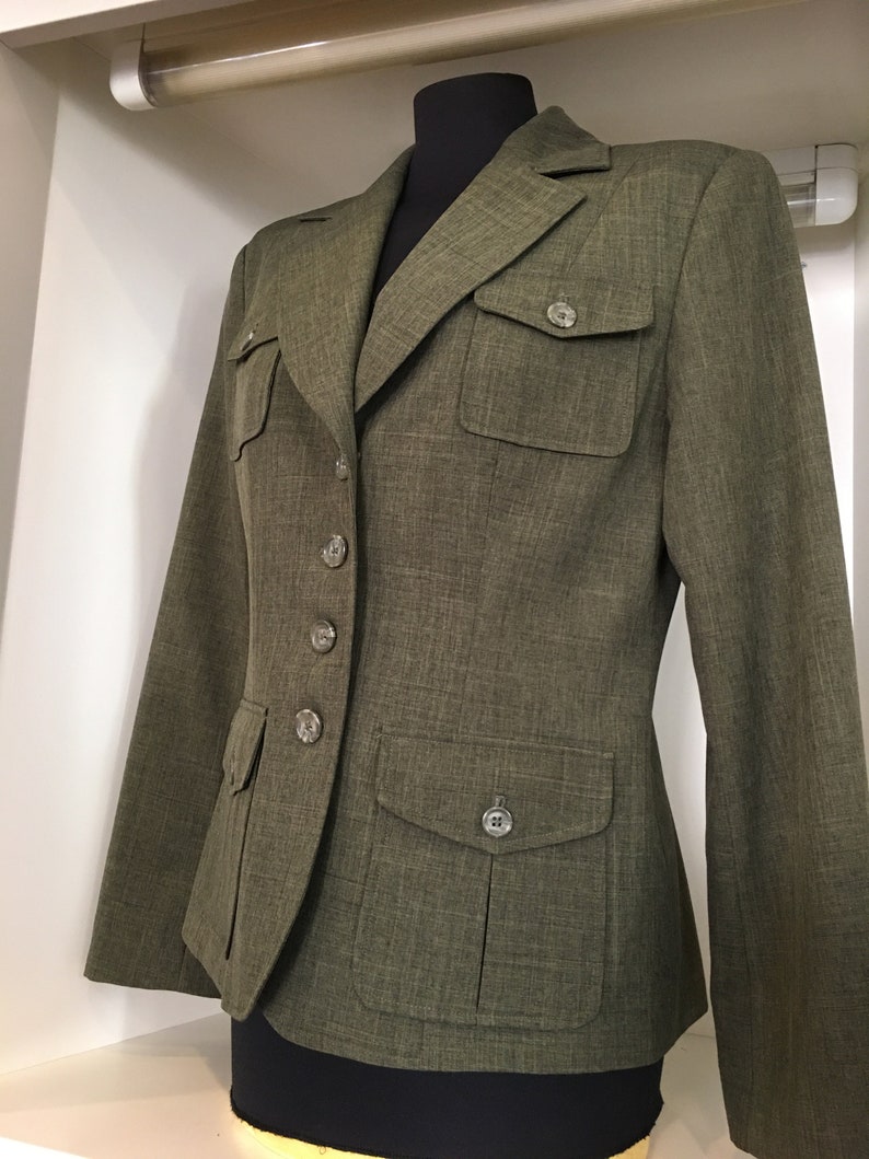 Op de afbeelding: Een groene blazer met knoopsluiting en twee grote zakken aan de voorkant. De blazer heeft een textuur in de stof en een aansluitende pasvorm.