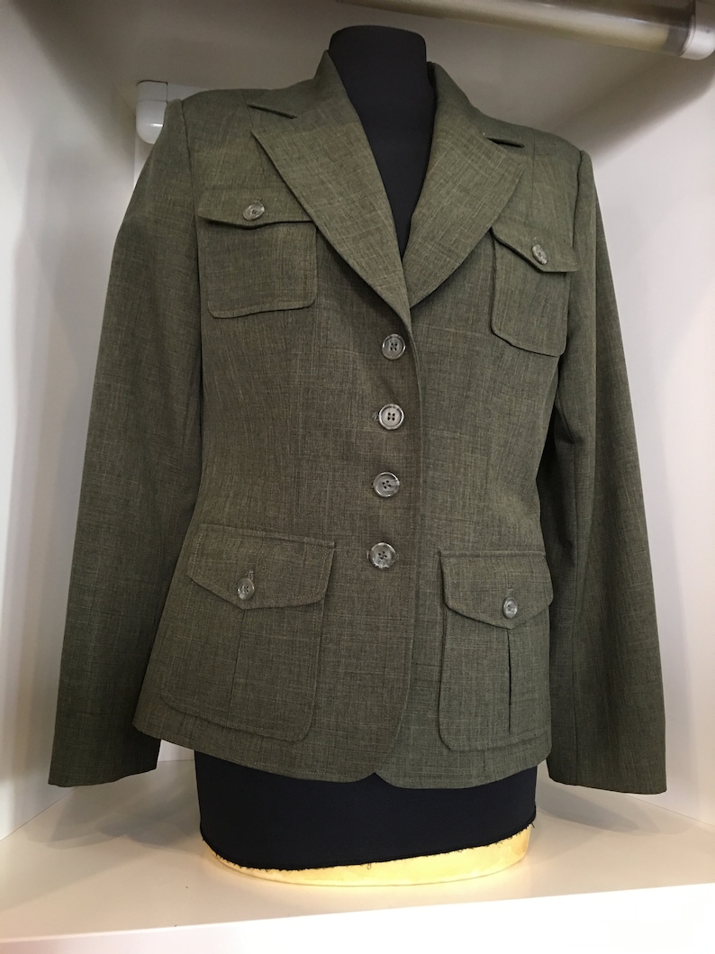 Op de afbeelding: Een groene blazer met vier knopen en twee grote klepzakken. De blazer heeft een reverskraag en lange mouwen.