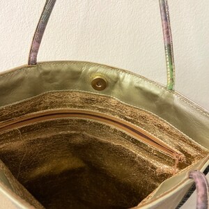 May include: The inside of a gold-coloured tote bag with a zipped pocket and a snap closure. The bag has a patterned strap.