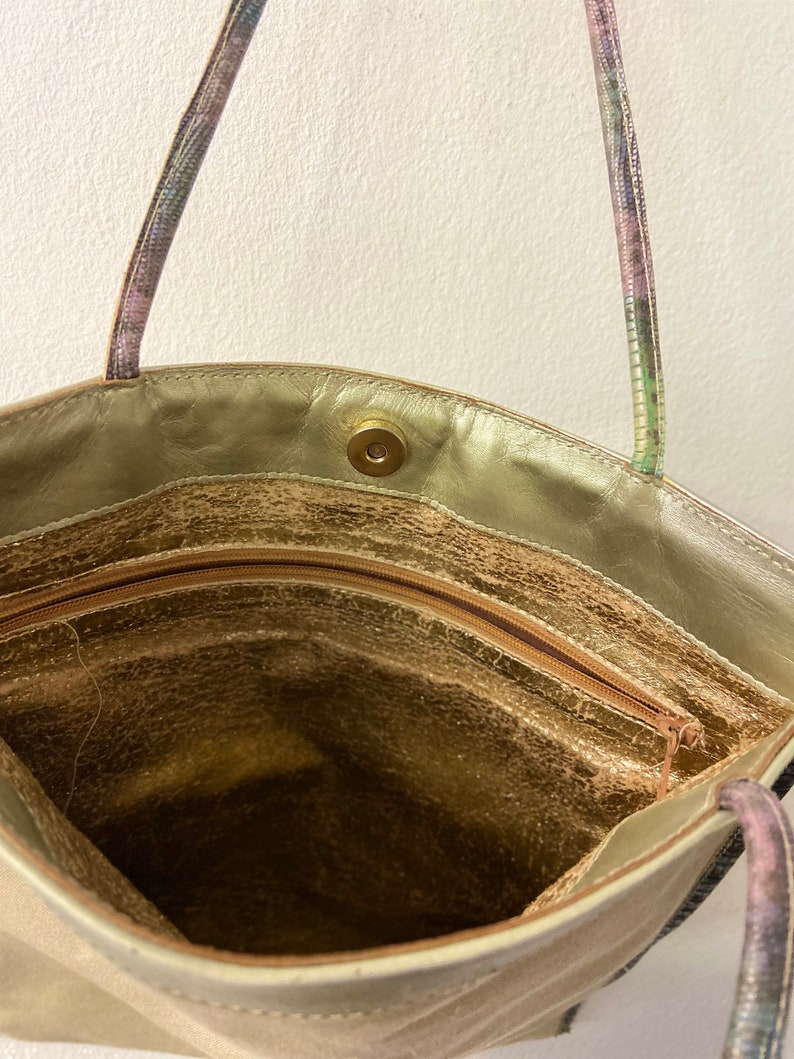 May include: The inside of a gold-coloured tote bag with a zipped pocket and a snap closure. The bag has a patterned strap.