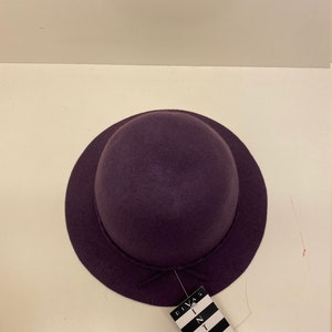 May include: A purple felt hat with a small brim and a bow on the front. The hat has a tag attached to it that says "Divas in Vintage Gallery".