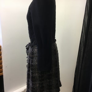 Puede incluir: Un vestido negro con falda con volantes y mangas largas. La falda est&aacute; hecha de una tela texturizada con un patr&oacute;n negro y gris.