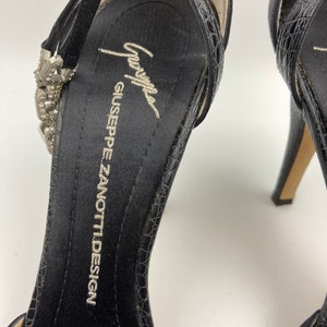 May include: Black satin high heel shoes with a jeweled ankle strap and a Giuseppe Zanotti Design label on the insole.