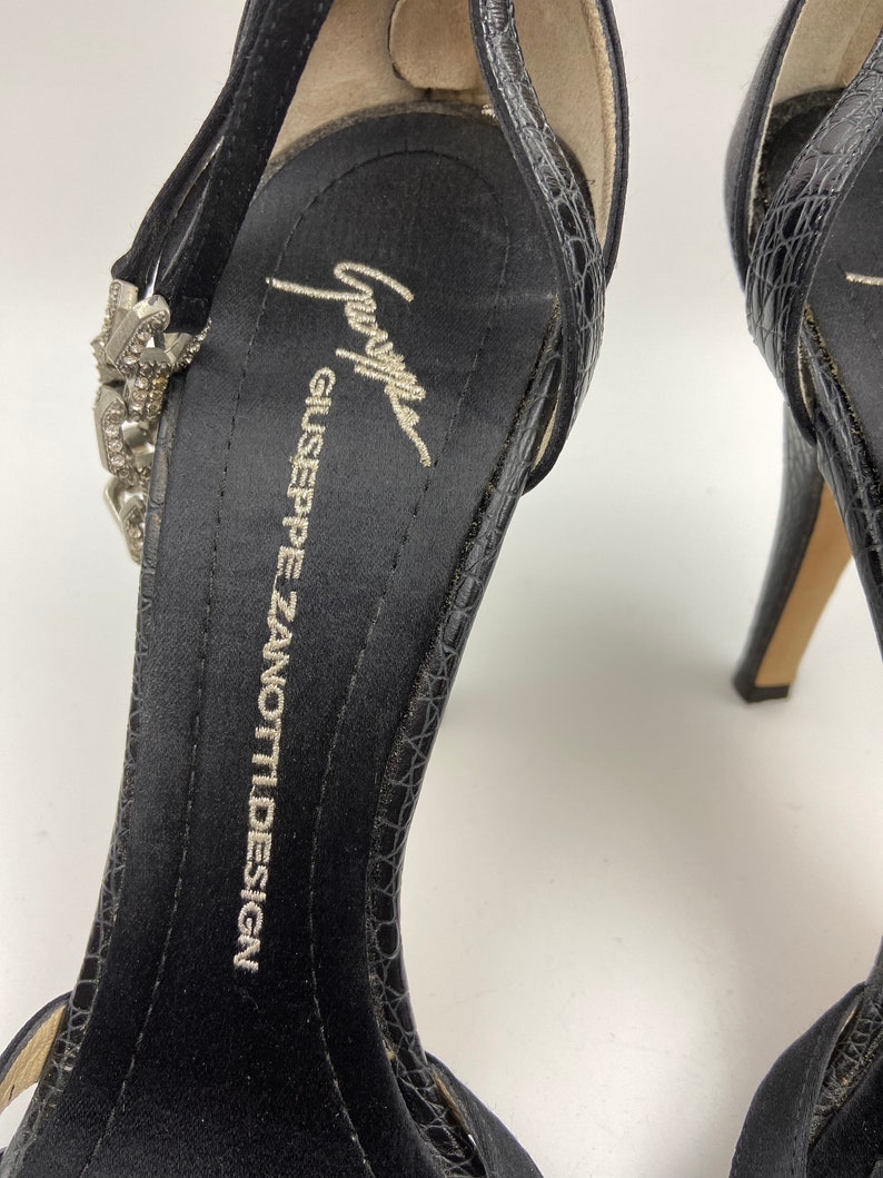 May include: Black satin high heel shoes with a jeweled ankle strap and a Giuseppe Zanotti Design label on the insole.